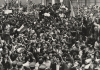 A black and white image of a crowd of people, the Chilean flag can be seen waving